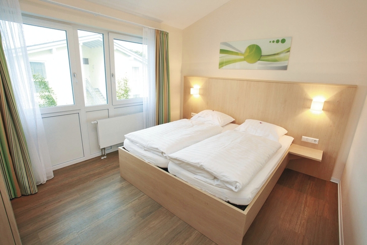 Helles Schlafzimmer mit Doppelbett und großem Fenster.