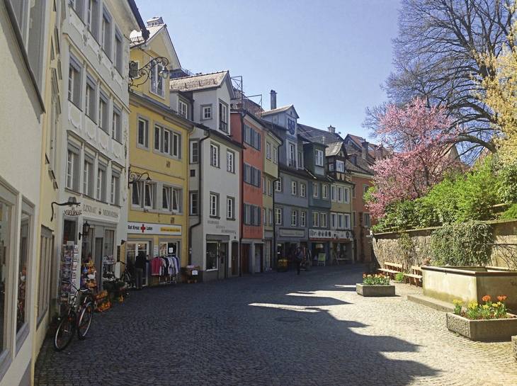 Straßenszene in Lindau mit bunten Häusern und blühendem Baum.
