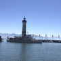 Ein Dampfschiff fährt vor einem Leuchtturm im Hafen, Berge im Hintergrund.