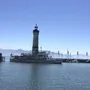 Ein Dampfschiff fährt vor einem Leuchtturm im Hafen, Berge im Hintergrund.