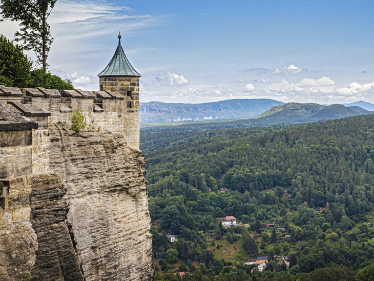 Festung Königstein mit Blick über bewaldete Hügel und das Elbsandsteingebirge.