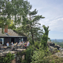 Terrasse einer Bergwirtschaft mit Gästen, Blick auf bewaldete Landschaft und Fernsicht.