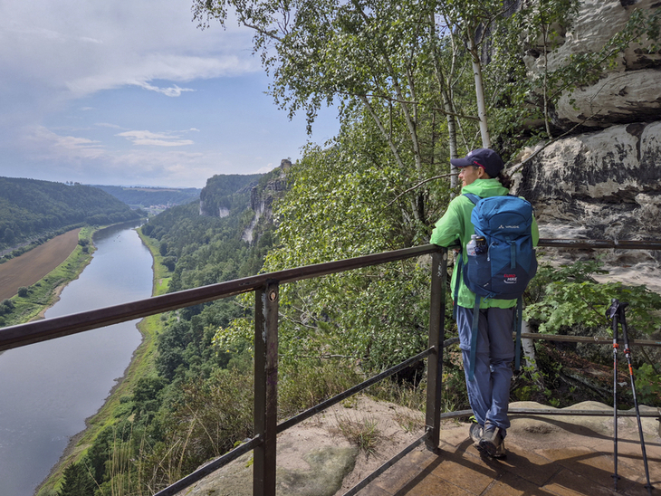 Wanderin auf Aussichtsplattform mit Blick auf Fluss und Felsen im Malerweggebiet.