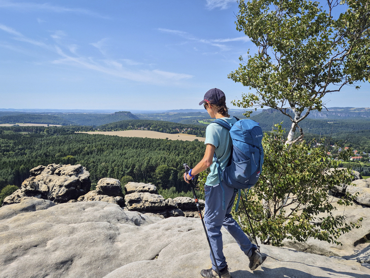 Wanderer mit Rucksack auf dem Malerweg mit Aussicht auf bewaldete Landschaft.