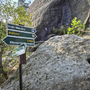 Wegweiser am Malerweg mit grünen Schildern und Felsen im Hintergrund.