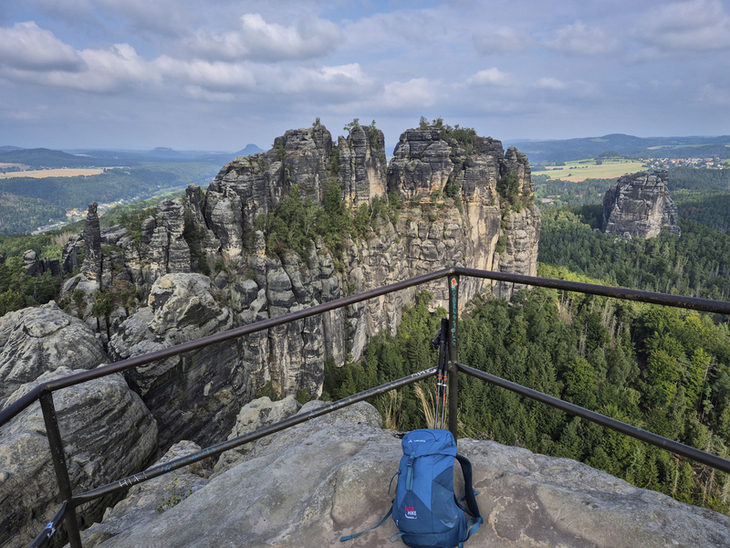 Blick von einer Aussichtsplattform auf Felsformationen des Malerwegs, mit Rucksack im Vordergrund.