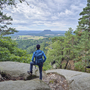 Person mit Blick auf bewaldete Landschaft und Lilienstein im Hintergrund.