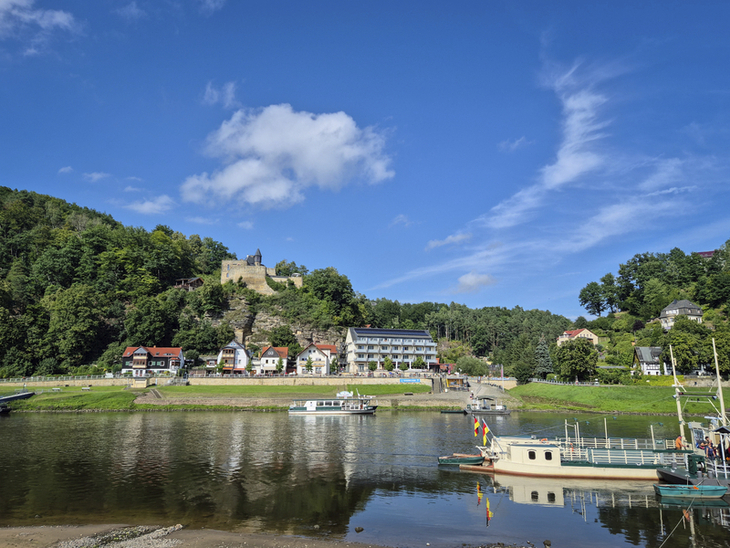 Fährstelle in Rathen mit Fluss, Booten und Hügel im Hintergrund.