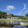 Fährstelle in Rathen mit Fluss, Booten und Hügel im Hintergrund.