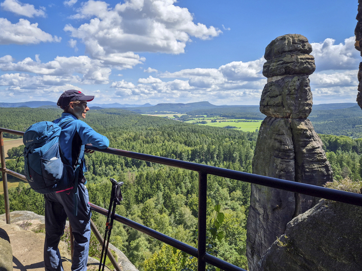 Eine Person wandert mit Rucksack und Wanderstöcken am Aussichtspunkt Pfaffenstein.