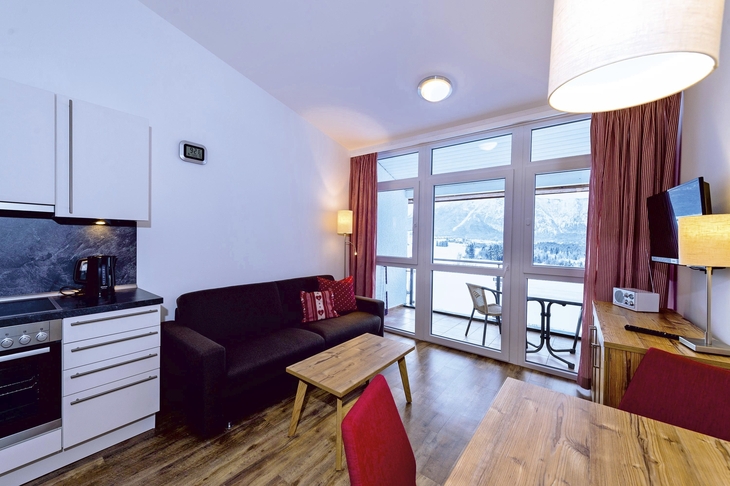 Wohnzimmer mit Küche in Ferienwohnung, Holzboden, Sofa und Fenster mit Bergblick.