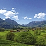 Landschaft bei Inzell mit Bergen und Wiesen unter blauem Himmel.