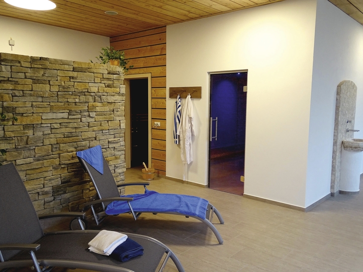 Ruheraum mit Liegestühlen, Bademänteln an der Wand und Natursteinwand.