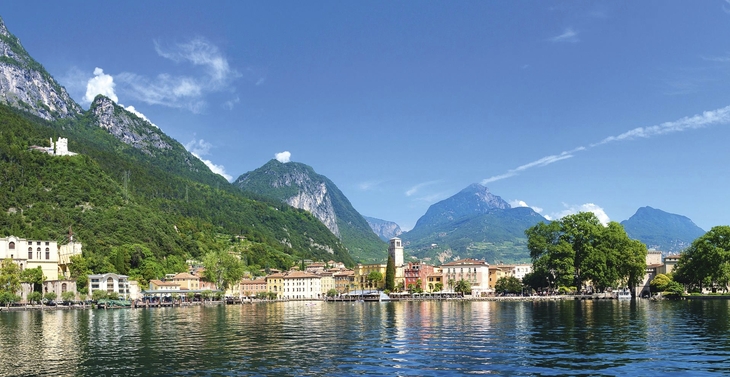 Stadt Riva del Garda am See mit Bergen im Hintergrund bei klarem Himmel.