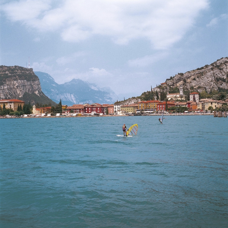 Surfer auf dem Gardasee vor Bergkulisse und bunten Häusern