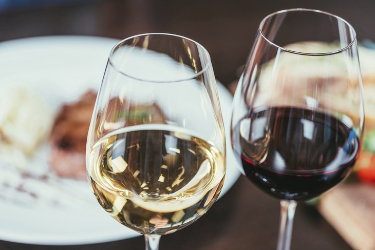 Zwei Weingläser mit weißem und rotem Wein auf einem Restauranttisch.