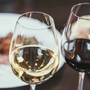 Zwei Weingläser mit weißem und rotem Wein auf einem Restauranttisch.