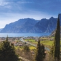 Blick auf den Gardasee mit Bergen im Hintergrund und Zypressen im Vordergrund.