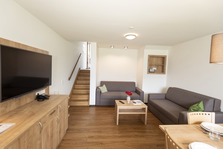Wohnzimmer eines Ferienhauses mit Sofa, Fernseher und Treppe.