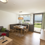 Wohnzimmer einer Ferienwohnung mit Esstisch, Sofa und großem Fenster mit Ausblick.