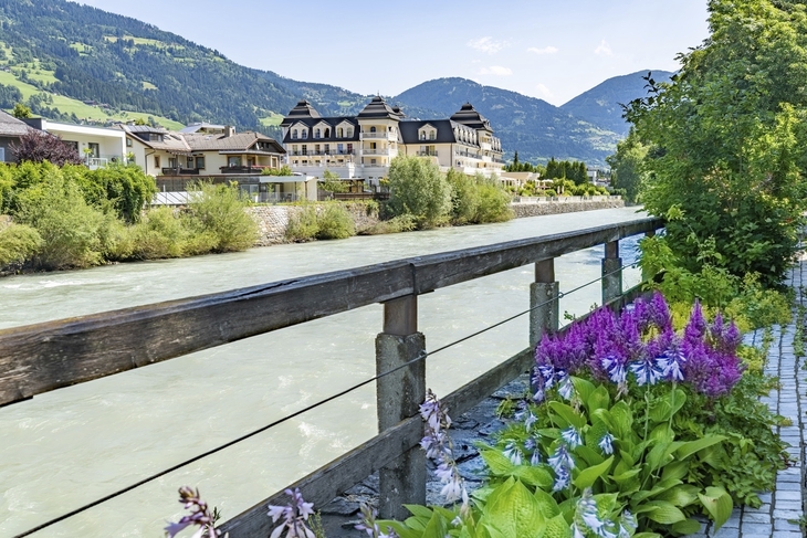 Fluss in Lienz, umgeben von Bergen und Gebäuden, mit Blumen im Vordergrund.
