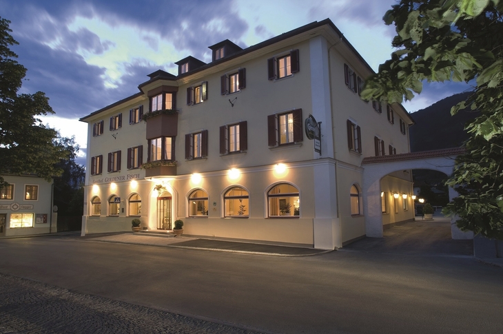 Beleuchtetes Hotelgebäude in der Dämmerung mit Bäumen im Vordergrund.