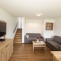 Wohnzimmer eines Ferienhauses mit Sofa, Fernseher und Treppe.