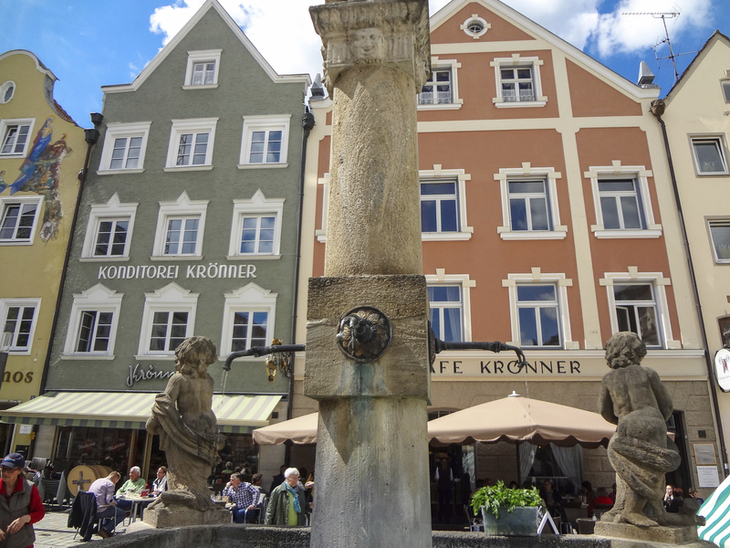 Historischer Brunnen vor bunten Häusern in einer bayerischen Stadt.