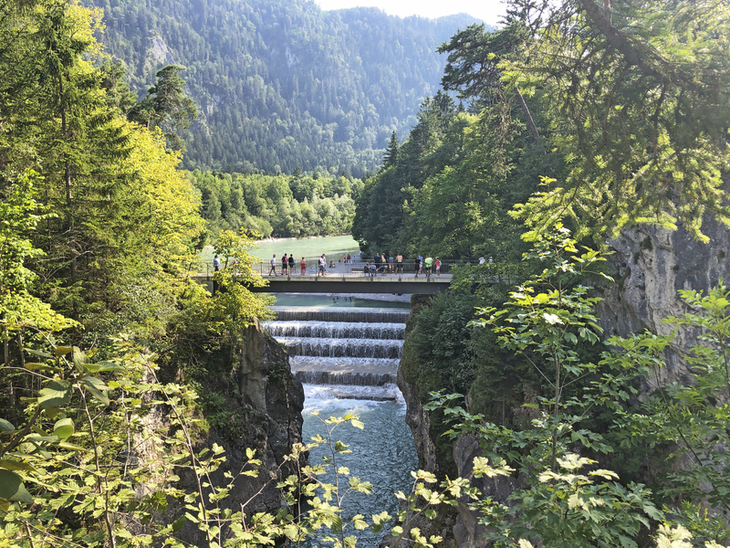 Brücke über einen Wasserfall in einer bewaldeten Berglandschaft auf dem Bayerischen Jakobsweg.