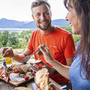Zwei Personen essen Brotzeit mit Bergblick und Weizenbier im Freien.