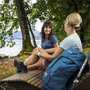 Zwei Wanderinnen sitzen auf einer Bank am Ufer und machen eine Pause.