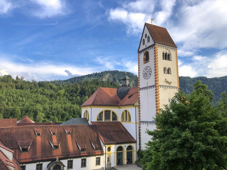 Kirche mit Turm vor bewaldeten Hügeln und blauem Himmel