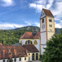 Kirche mit Turm vor bewaldeten Hügeln und blauem Himmel