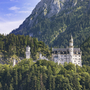 Schloss Neuschwanstein vor bewaldeten Bergen im Sonnenschein.