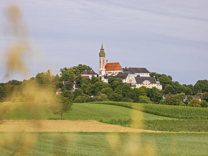 Landschaft mit Kirche und Kloster auf Hügel, umgeben von Feldern und Bäumen.