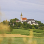 Landschaft mit Kirche und Kloster auf Hügel, umgeben von Feldern und Bäumen.