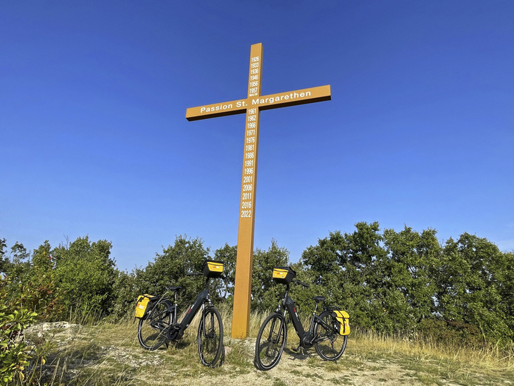 Zwei Fahrräder vor einem großen Holzkreuz im Freien bei klarem Himmel.