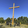 Zwei Fahrräder vor einem großen Holzkreuz im Freien bei klarem Himmel.