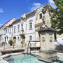 Häuserzeile in Eisenstadt mit historischem Brunnen und blauem Himmel.