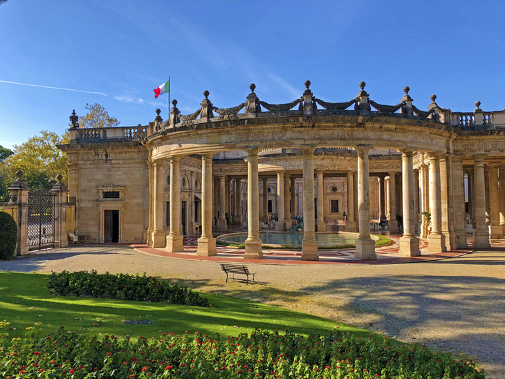 Historisches Gebäude mit Säulen und italienischer Flagge im Hintergrund.