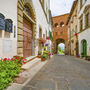 Blick auf ein historisches Stadttor in Montecarlo mit Blumen und alten Gebäuden.