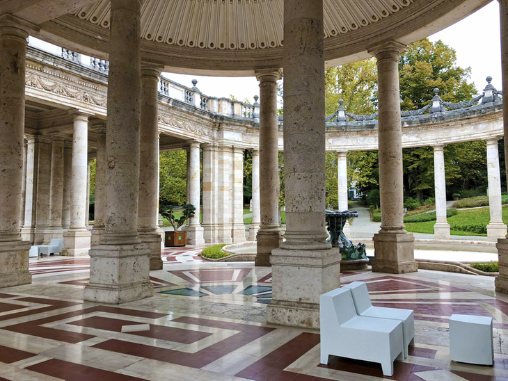 Säulenhalle der Terme Tettuccio mit Sitzgelegenheiten und Gartenansicht.