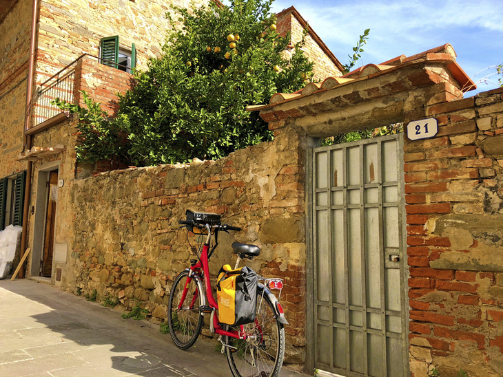Fahrrad vor steinernem Haus und Garten, sonniger Tag in Vinci, Italien.