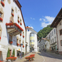 Straßenansicht im Zentrum von Mals mit historischen Gebäuden und Blumenschmuck.