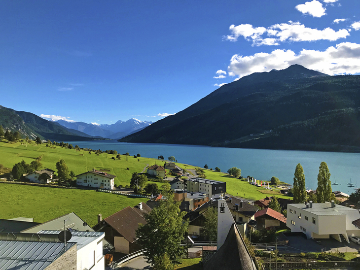 Dorf und Reschensee vor Bergkulisse bei klarem Himmel.