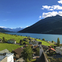 Dorf und Reschensee vor Bergkulisse bei klarem Himmel.