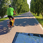 Radfahrer auf baumgesäumtem Weg mit Karte im Vordergrund.