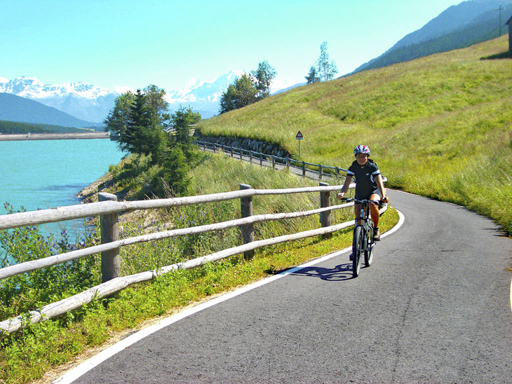 Radfahrer auf einem malerischen Weg am Reschensee mit Bergen im Hintergrund