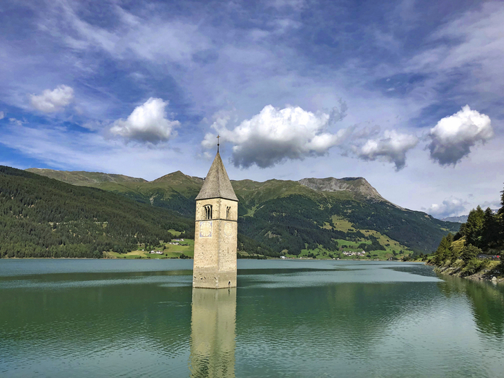 Kirchturm in Reschensee mit Bergen im Hintergrund bei klarem Himmel.