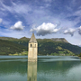 Kirchturm in Reschensee mit Bergen im Hintergrund bei klarem Himmel.